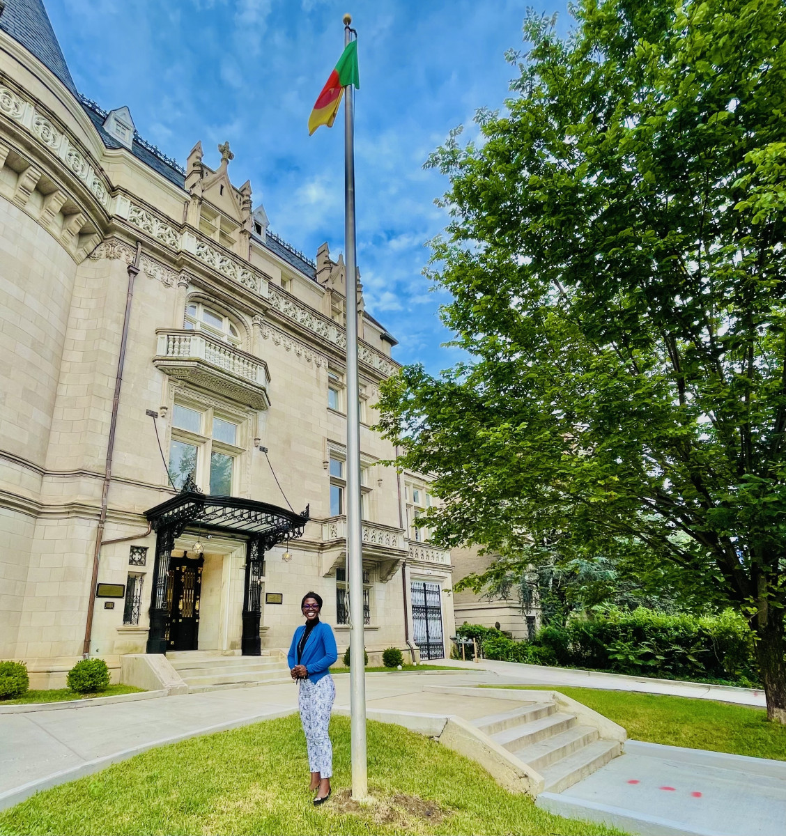 Beverly stands under the Cameroonian flag in front of the Cameroon embassy building in Washington D.C.